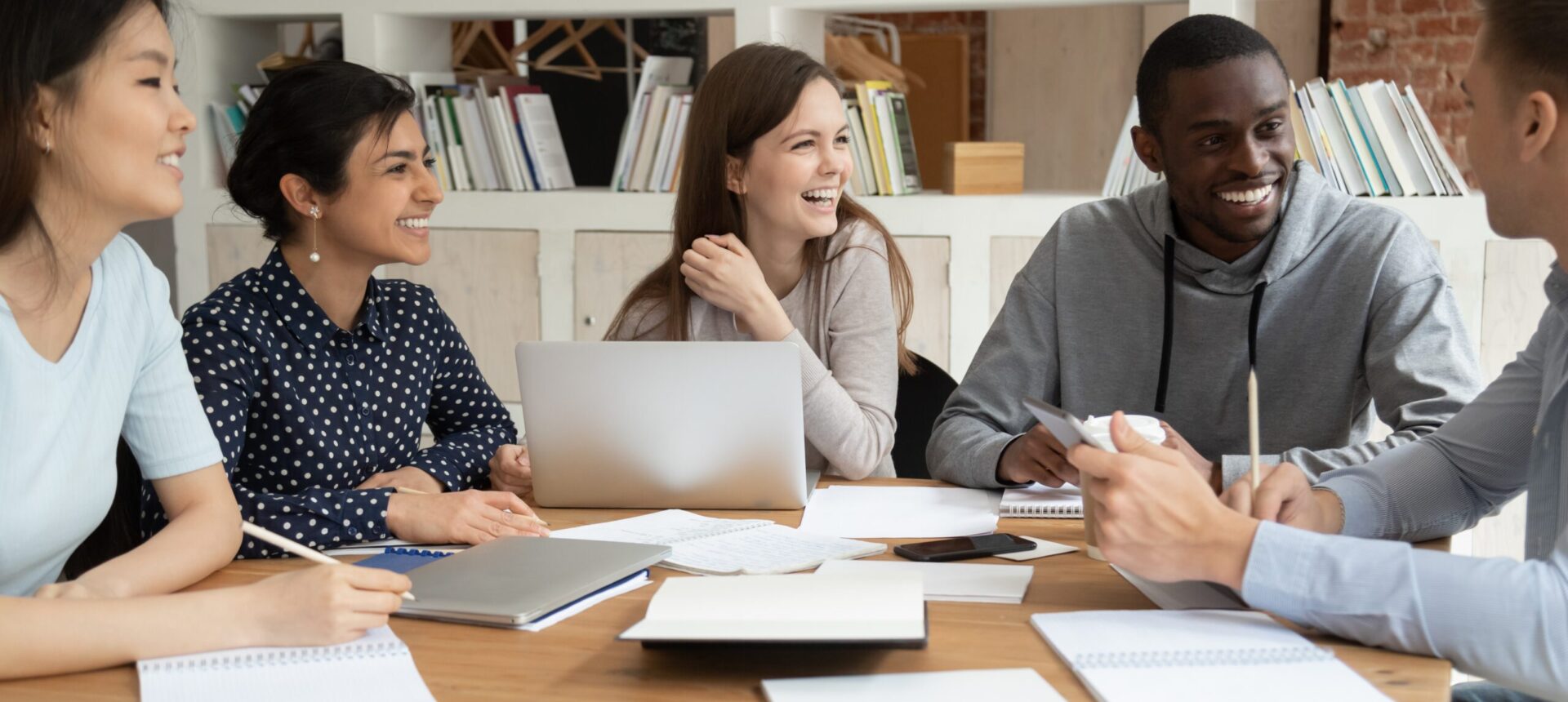 Overjoyed,Multiracial,Young,People,Sit,At,Table,With,Laptop,And